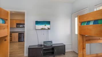 A room with bunk beds, a TV on the wall, a small cabinet, and a kitchen area in the background.