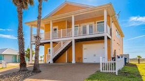 A two-story house with a covered porch, a garage, and a staircase leading to the upper level. - Pier Pressure Pools Beach Access Sunset View (Port Aransas)