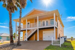 A two-story house with a covered porch, a garage, and a staircase leading to the upper level. - Pier Pressure Pools Beach Access Sunset View (Port Aransas)