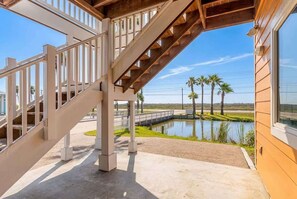 A staircase leading to a covered outdoor area with a view of a lake and palm trees. - Pier Pressure Pools Beach Access Sunset View (Port Aransas)