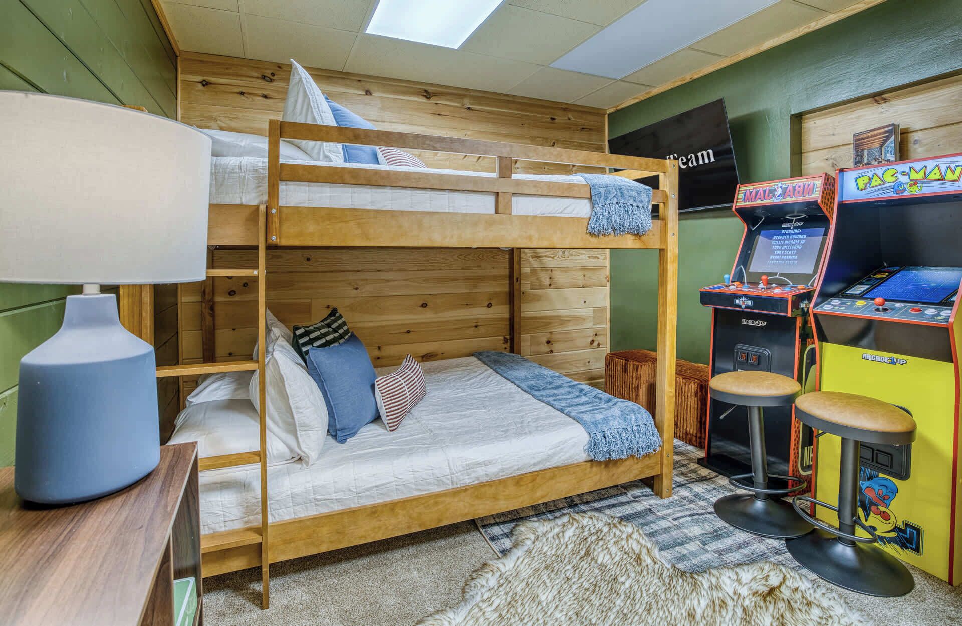 A bunk bed room with a Pac-Man arcade machine and a lamp.