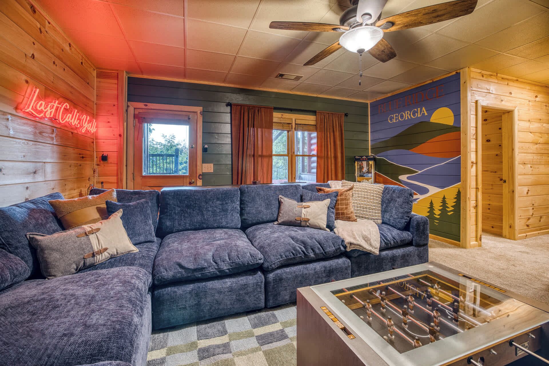 A cozy room with a blue sofa, a foosball table, and a mural of Georgia's Blue Ridge Mountains.