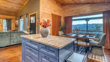 A wooden interior with a kitchen island, dining area, and a view through large windows.