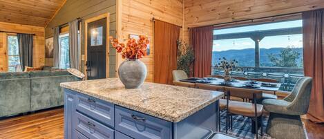 A wooden interior with a kitchen island, dining area, and a view through large windows.
