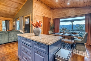 A wooden interior with a kitchen island, dining area, and a view through large windows.