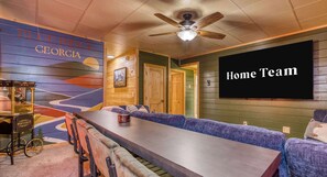 A cozy room with a long table, a popcorn machine, a large TV screen, and a mural on the wall.