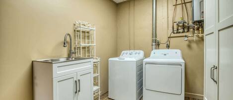 A laundry room with a sink, two washing machines, and a metal rack.