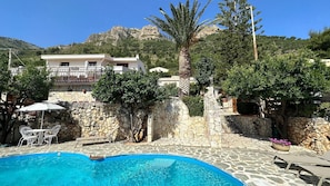 A pool area with stone flooring, lounge chairs, and a white building in the background. - Charming Holiday Home Near Sea (Castellammare del Golfo)