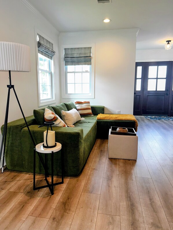 Una sala de estar con un sofá seccional verde, una lámpara de pie, una mesita con una vela y un banco de madera.
