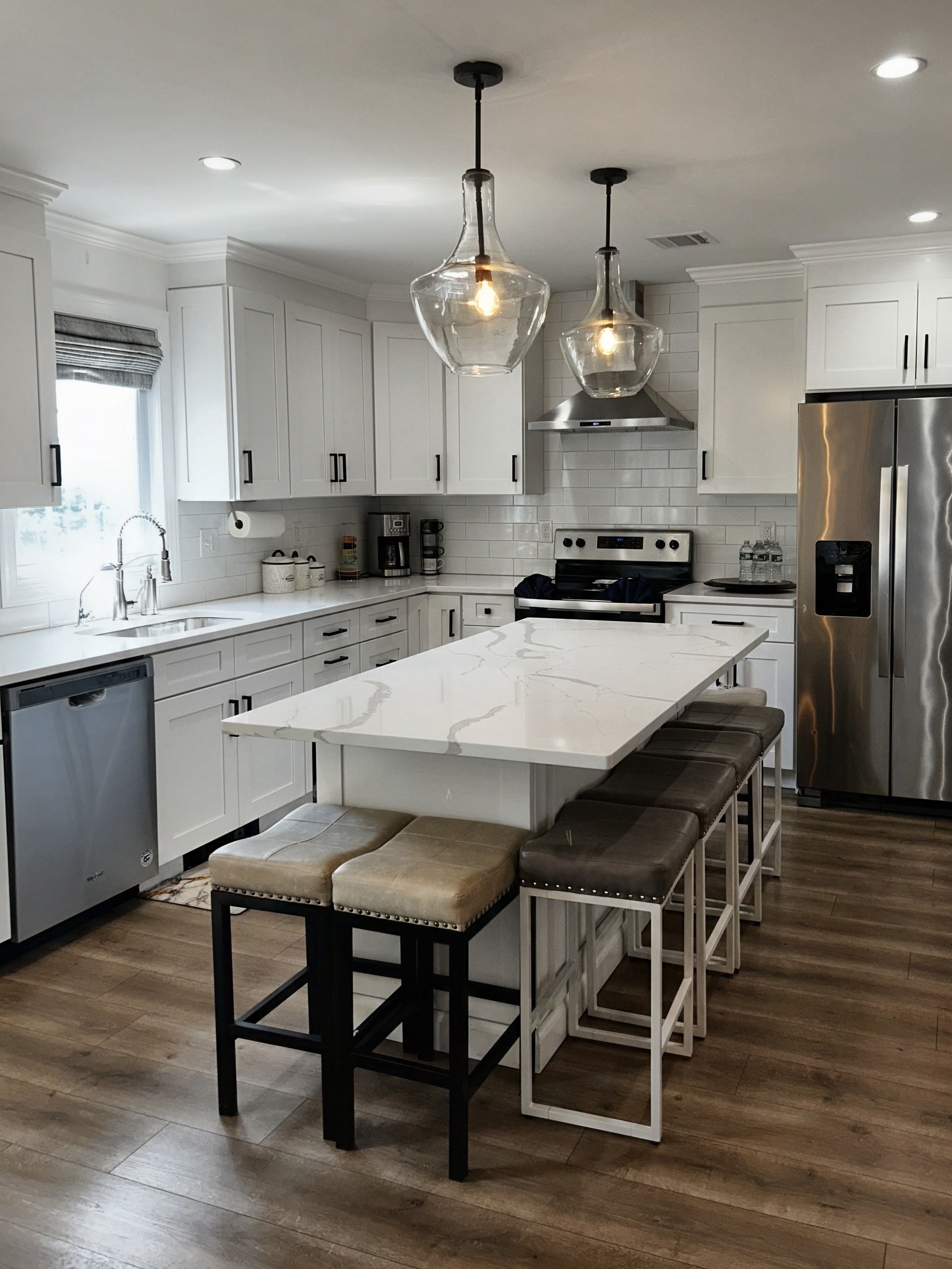 A modern kitchen with white cabinetry, a central island with bar stools, stainless steel appliances, and pendant lighting.