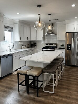 A modern kitchen with white cabinetry, a central island with bar stools, stainless steel appliances, and pendant lighting. - Lux Lakeview Experience Sleep 8 (Hopatcong)