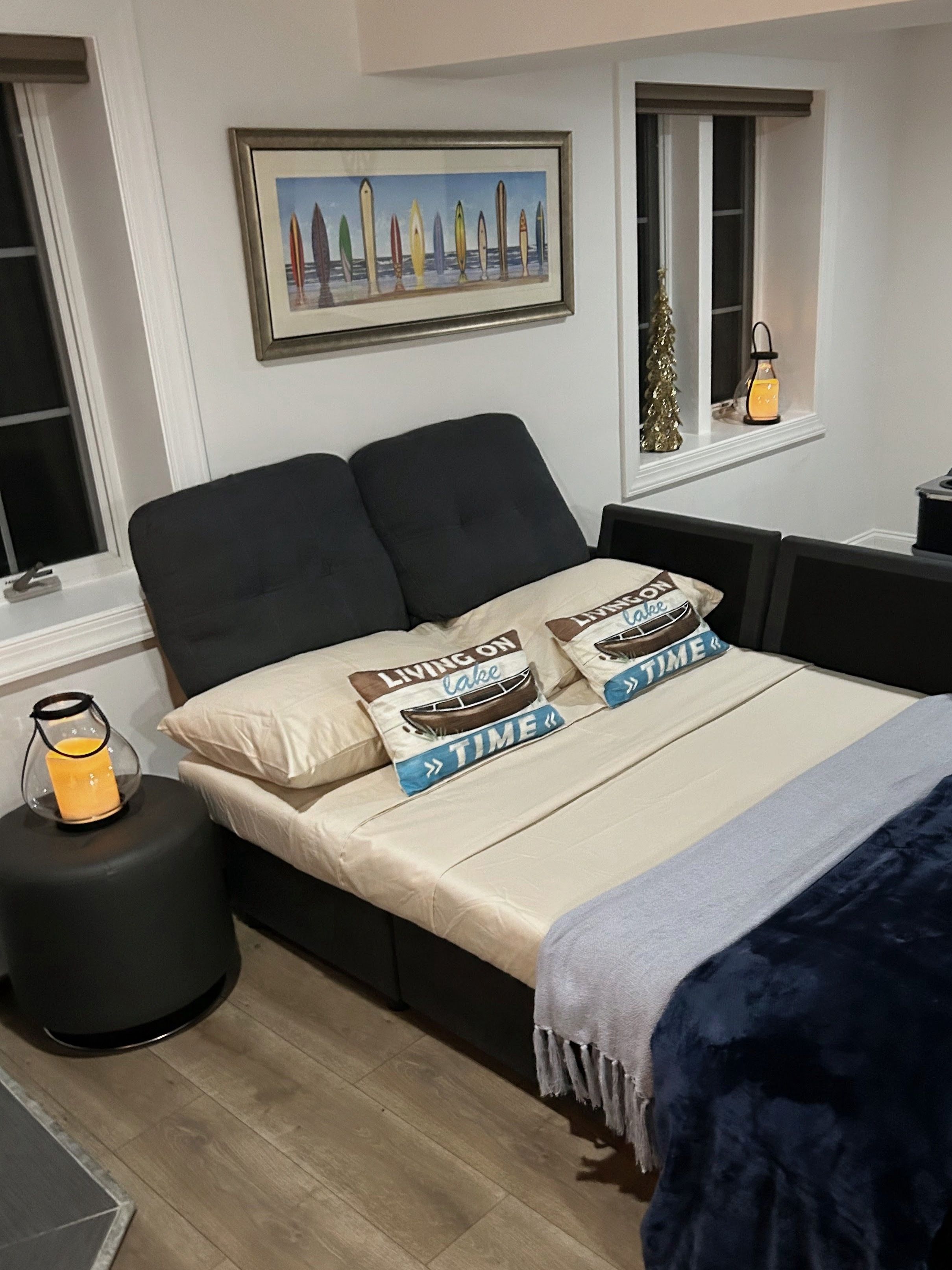 A bedroom with a bed, a window with a view, a framed picture on the wall, and a bedside table with a candle.