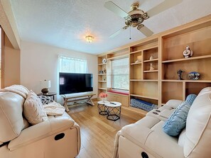 Ein Wohnzimmer mit Flachbildfernseher, Ledersofas, Deckenventilator und Einbauschränken.
