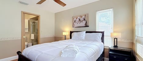 A bedroom with a bed, a ceiling fan, a window with blinds, a nightstand, and a wall-mounted picture.