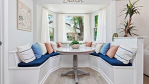 A bay window seating area with a round table, cushioned benches, and a potted plant. - Cayuga Clubhouse • Poolside Fun & Game Room (Jacksonville)