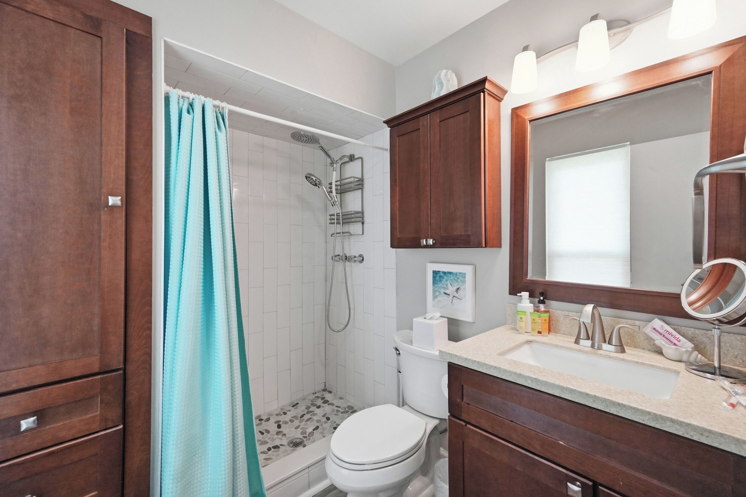 A bathroom with a shower, toilet, vanity, and a large mirror.