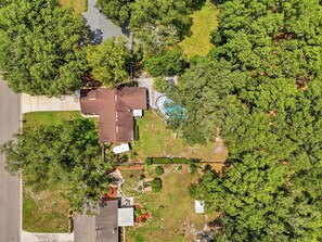 An aerial view of a residential area with a house, a swimming pool, and surrounding greenery. - Cayuga Clubhouse • Poolside Fun & Game Room (Jacksonville)