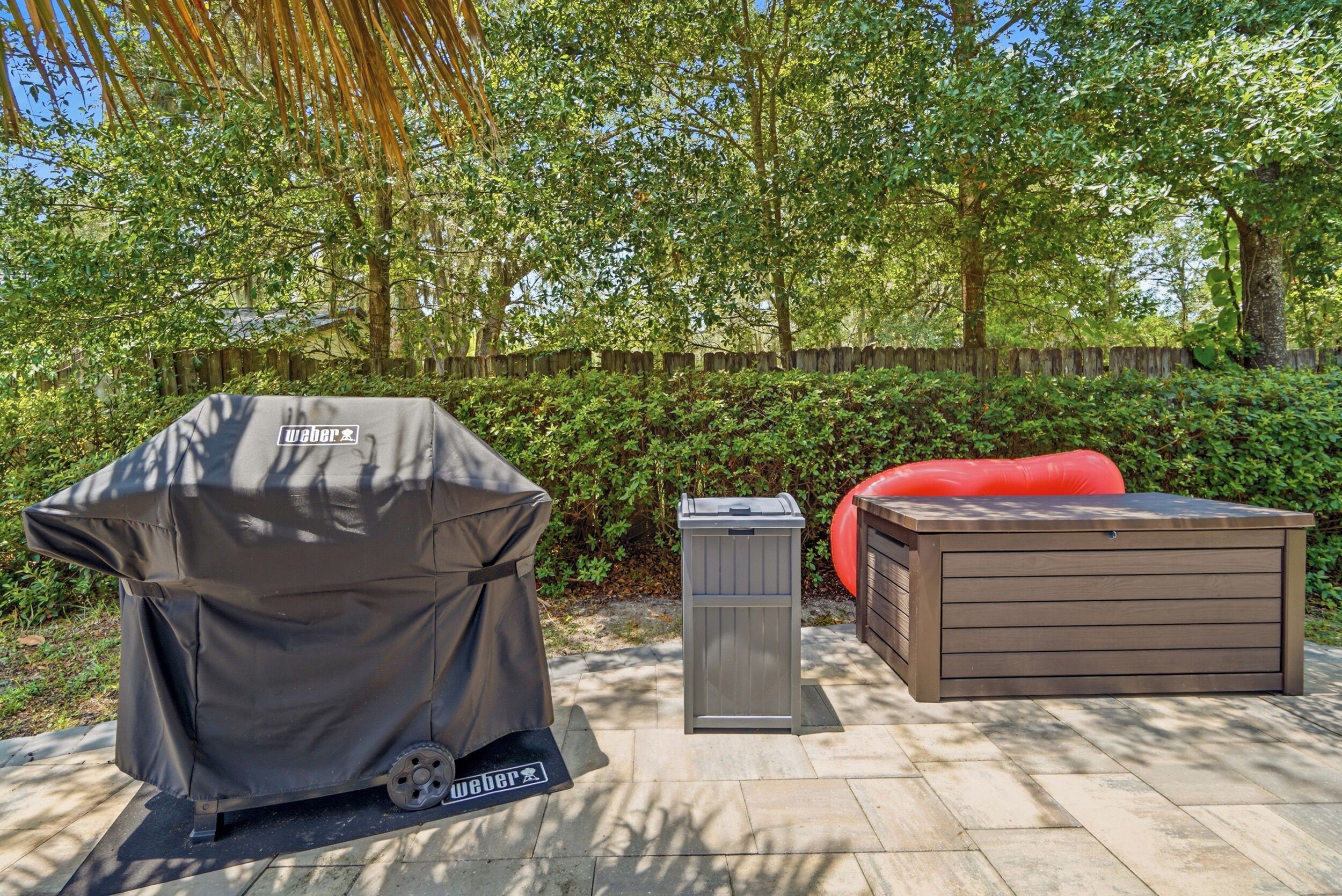 An outdoor barbecue grill, a trash can, and a wooden bench in a garden setting.