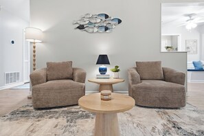 A modern living room with two armchairs, a round coffee table, a lamp, and a decorative wall piece. - Cayuga Clubhouse • Poolside Fun & Game Room (Jacksonville)