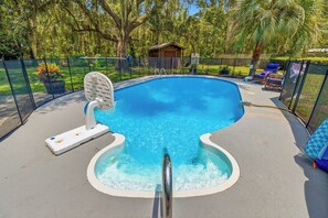 Ein Schwimmbecken mit Whirlpool, umgeben von einem Zaun und Bäumen.