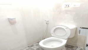 Et lille, hvidt toilet med lukket låg, en vægmonteret papirholder og et flisebelagt gulv.