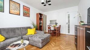 A living room with a grey sofa, a dining table with chairs, a bookshelf, and a TV on a cabinet. - House in Landunvez Near Penfoul Beach (Warsaw)