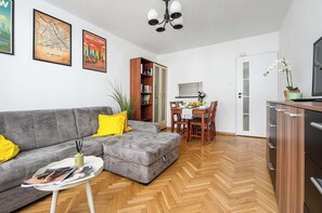 Ein Wohnzimmer mit grauem Sofa, einem Esstisch mit Stühlen, einem Bücherregal und einem Fernseher auf einer Kommode.