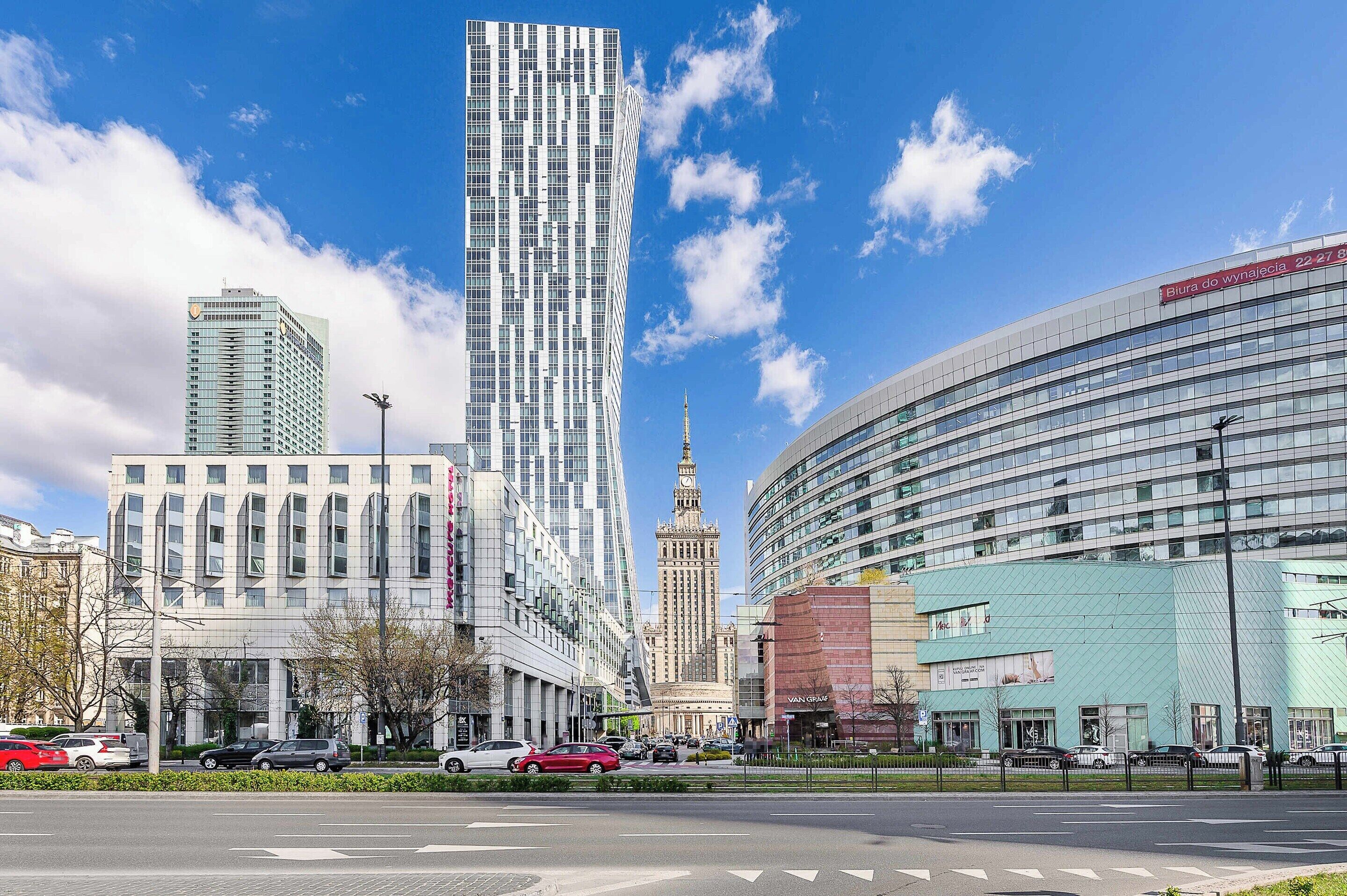 A cityscape with modern buildings, a prominent tower, and a street with cars.