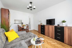 A modern living room with a grey sofa, a dining table with chairs, a TV, and a wooden cabinet with drawers. - House in Landunvez Near Penfoul Beach (Warsaw)