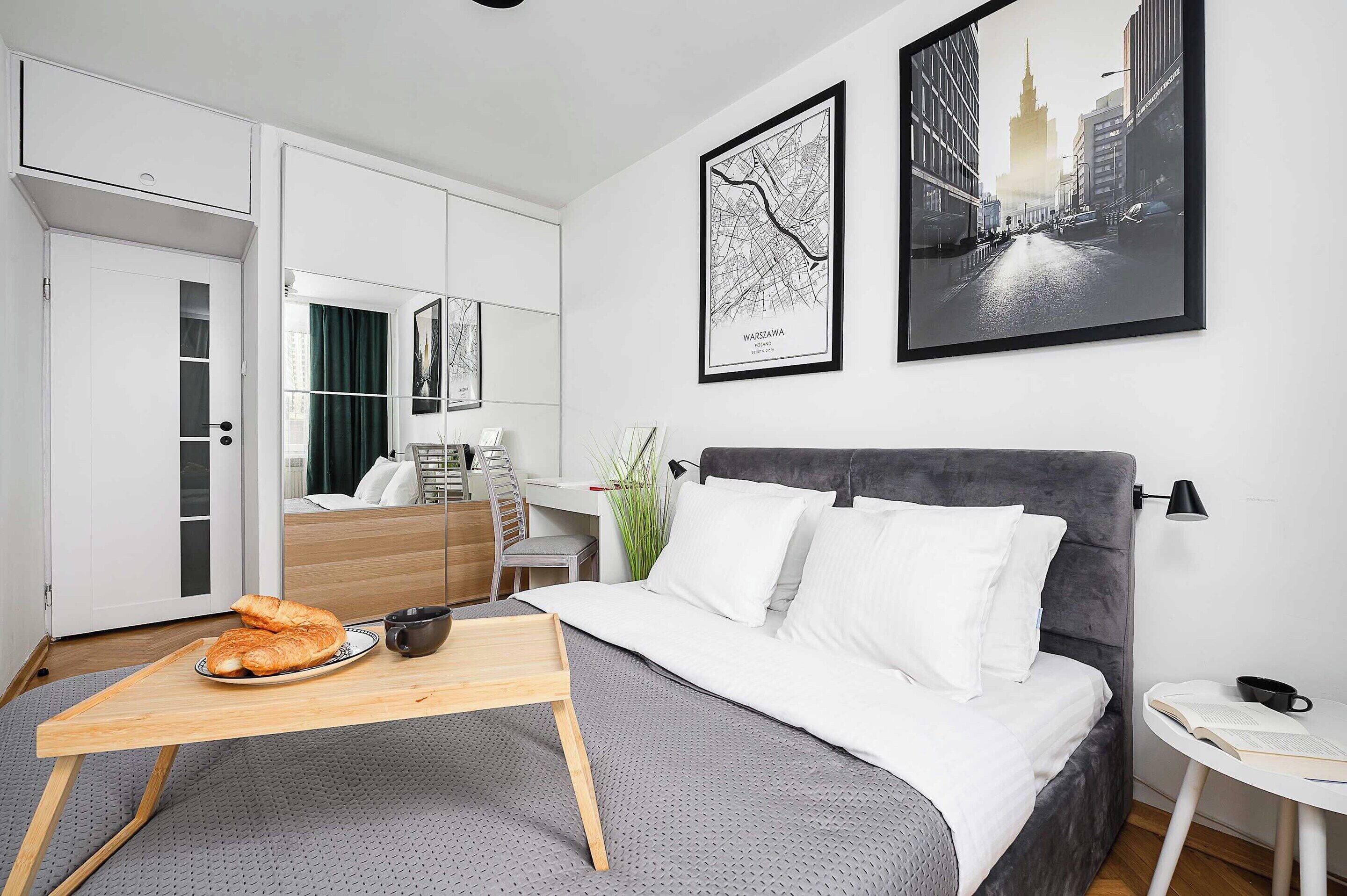Une chambre d’hôtel moderne, équipée d’un lit, d’un bureau, d’une chaise, d’une table à manger avec de la nourriture, et ornée d’œuvres d’art sur les murs.