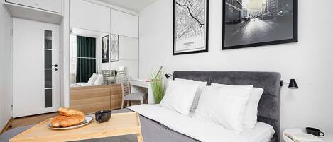 Une chambre d’hôtel moderne, équipée d’un lit, d’un bureau, d’une chaise, d’une table à manger avec de la nourriture, et ornée d’œuvres d’art sur les murs.