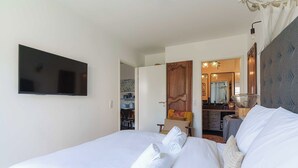 A hotel room with a bed, a flat-screen TV mounted on the wall, a wooden door, and a mirror. - Flat in the Heart of Deauville With a Garden (Deauville)