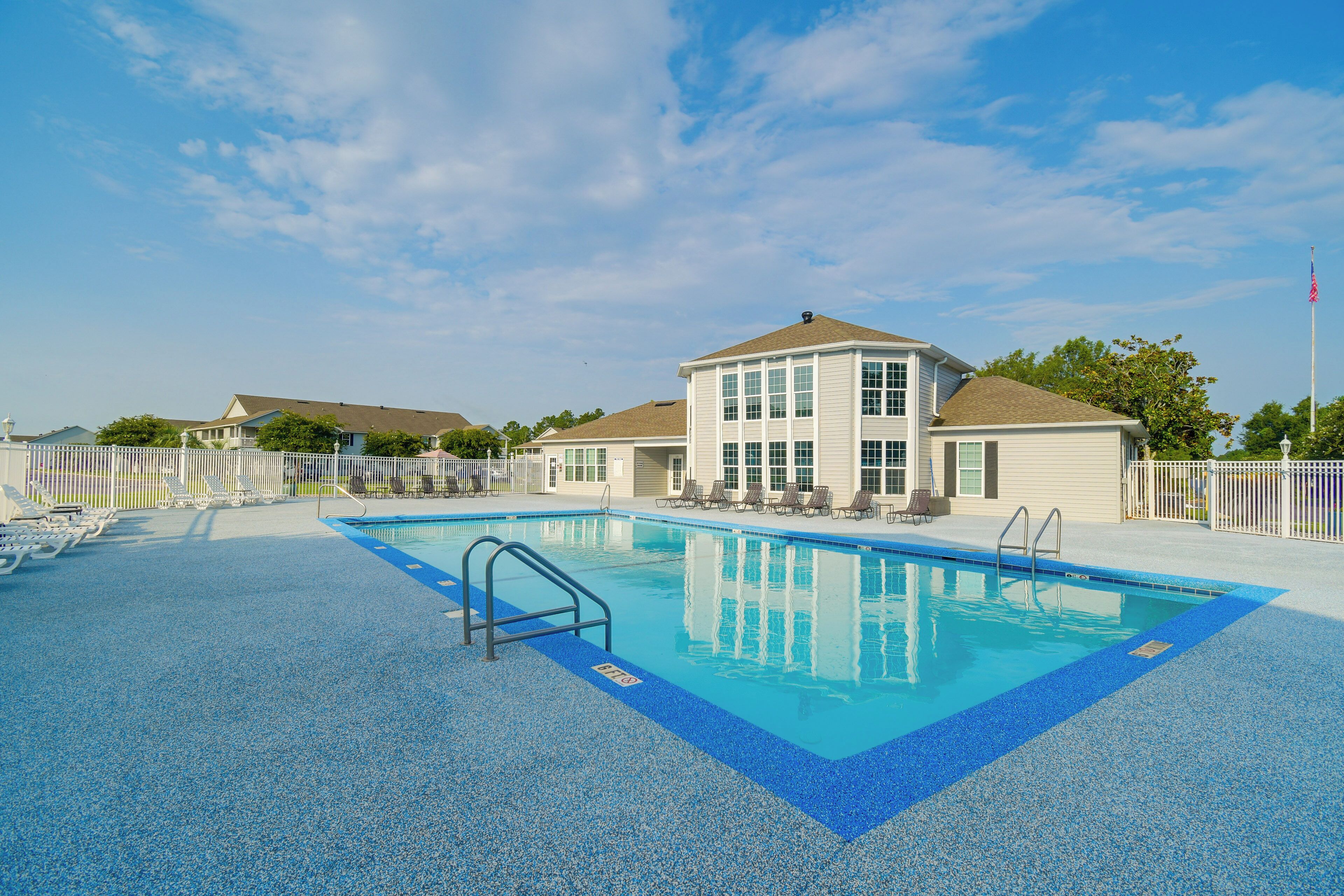 Ein Swimmingpool mit klarem, blauen Wasser, umgeben von Liegestühlen und einem Gebäude mit weißer Fassade.