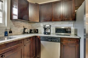 A kitchen with dark wood cabinets, a stainless steel dishwasher, a coffee maker, and a microwave. - Easy NYC Commute: Furnished Jersey City Home (Jersey City)