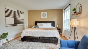 A bedroom with a bed, bedside table, lamp, and a blue chair. - Easy NYC Commute: Furnished Jersey City Home (Jersey City)