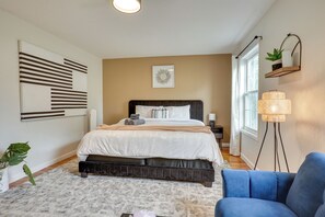 A bedroom with a bed, bedside table, lamp, and a blue chair. - Easy NYC Commute: Furnished Jersey City Home (Jersey City)