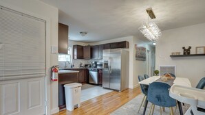 A modern kitchen with stainless steel appliances, wooden cabinets, and a dining area with a table and chairs. - Easy NYC Commute: Furnished Jersey City Home (Jersey City)