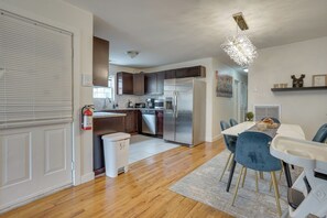 A modern kitchen with stainless steel appliances, wooden cabinets, and a dining area with a table and chairs. - Easy NYC Commute: Furnished Jersey City Home (Jersey City)