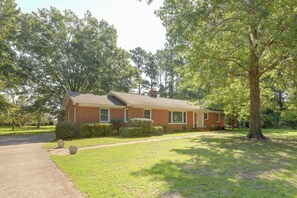 A single-story brick house with a front porch, surrounded by a well-maintained lawn and mature trees. - Back Deck, Grill, Yard! New Bern Family Home (New Bern)