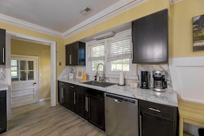 A kitchen with dark cabinets, a marble countertop, a dishwasher, and a coffee maker. - Back Deck, Grill, Yard! New Bern Family Home (New Bern)