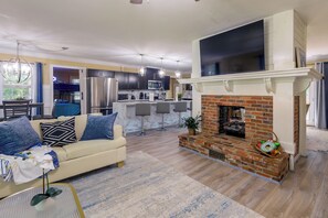 A modern living room with a fireplace, a sofa, and a dining area with a kitchen in the background. - Back Deck, Grill, Yard! New Bern Family Home (New Bern)
