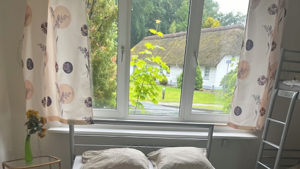 A single-bed room with a window, a bedside table with a vase, and a radiator. - Sleep in Filskov (Filskov)