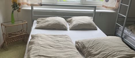 A single-bed room with a window, a bedside table with a vase, and a radiator.