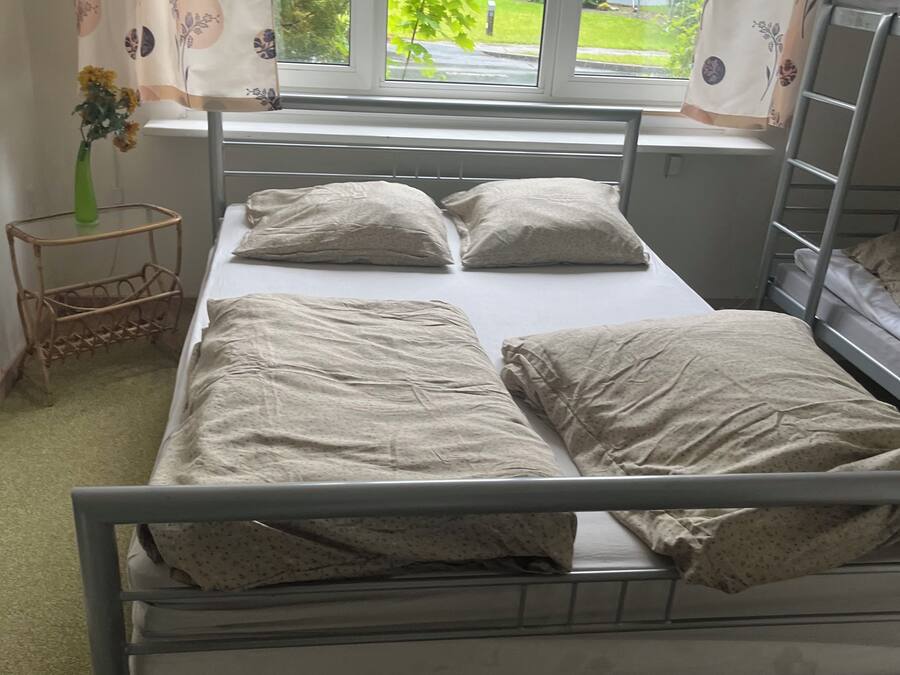 Een eenpersoonskamer met een raam, een nachtkastje met een vaas en een radiator.