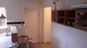 A kitchen with a white door, a wooden cabinet with glass doors, a hanging pendant light, and a vase with flowers on the counter. - Sleep in Filskov (Filskov)