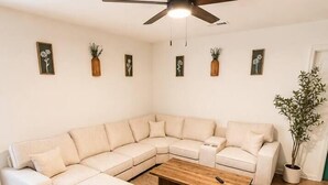 Een moderne woonkamer met een hoekbank, een houten salontafel en een plafondventilator.