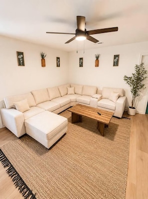 A modern living room with a sectional sofa, a wooden coffee table, and a ceiling fan. - The Sumerville's Carriage House (Summerville)