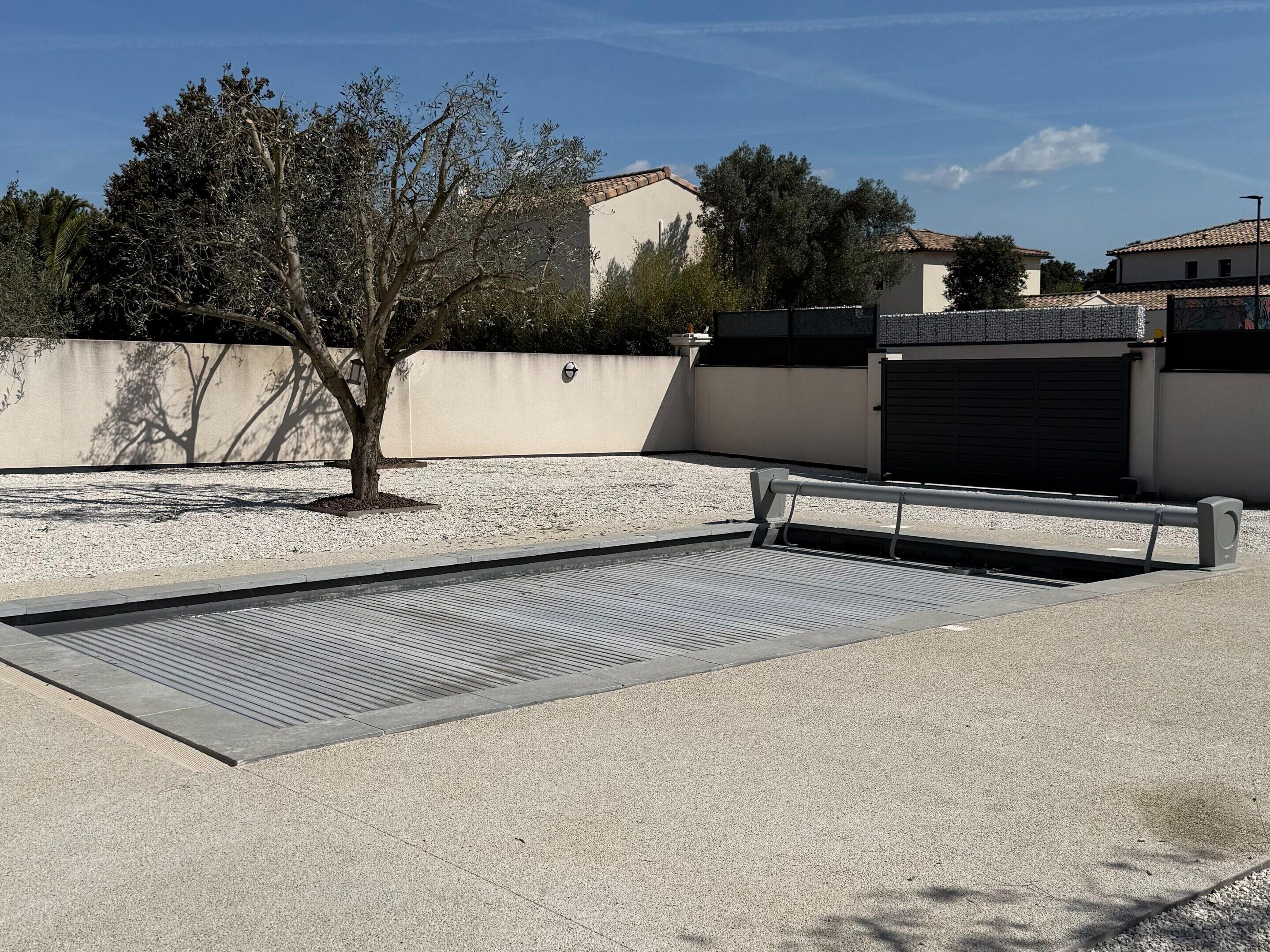 A swimming pool with a tiled deck, surrounded by a low wall and trees.