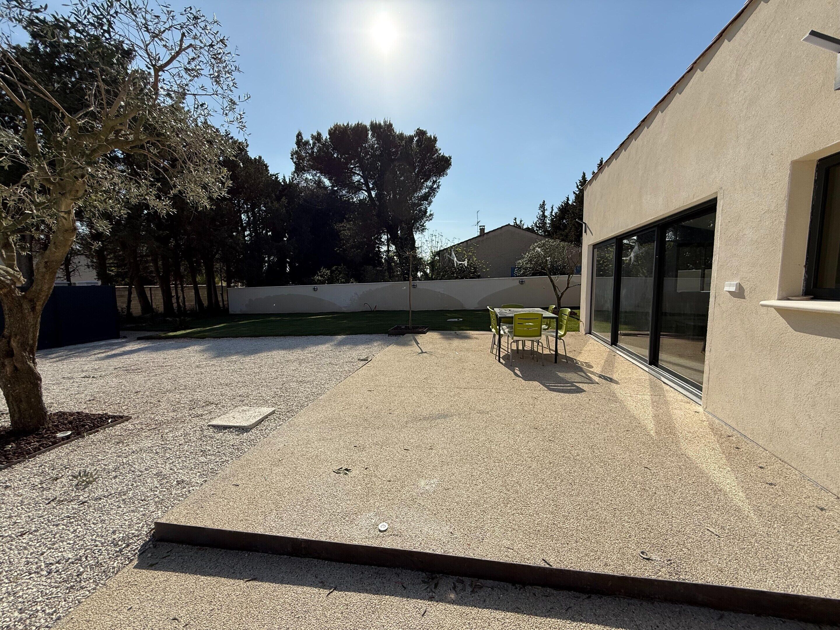 An outdoor patio area with a table and chairs, a gravel ground, and a building with large windows.