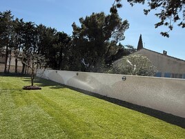 Uma área com grama, um muro baixo e árvores.